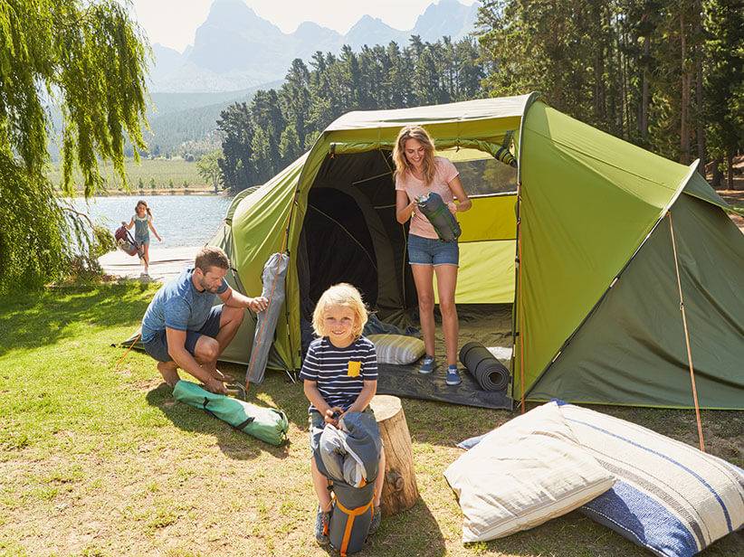 Familie auf Campingplatz, grünes Zelt aufgebaut, Schlafsäcke.