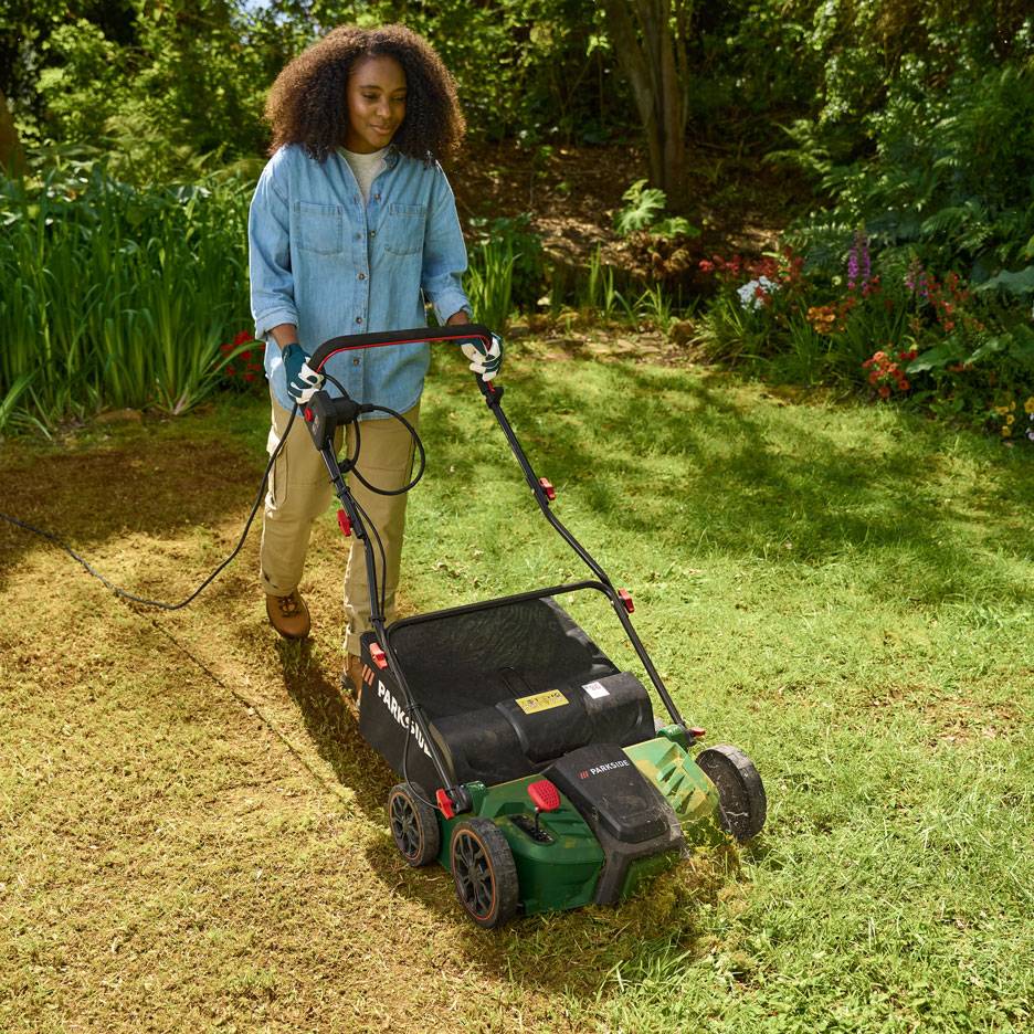 Frau benutzt einen elektrischen Rasenlüfter im Garten.