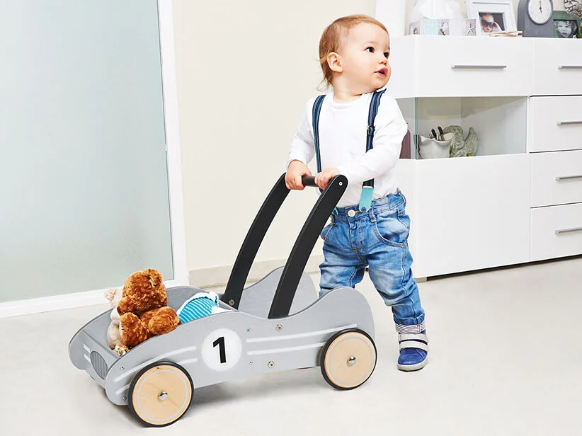 Kleinkind mit Lauflernwagen und Stofftier.