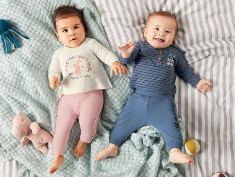 Zwei Babys in süßen Outfits; Mädchen mit Hasen-Shirt und Hose, Junge mit gestreiftem Shirt und Hose.