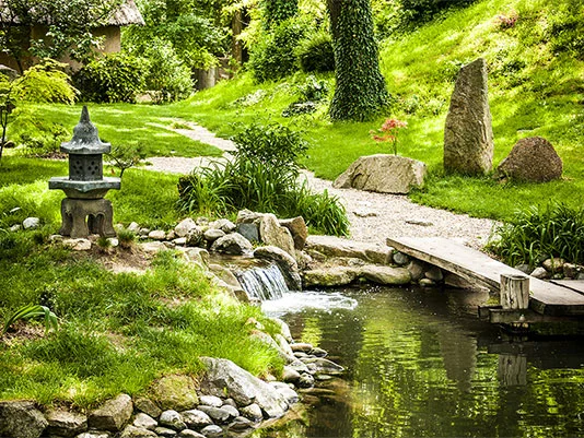 Japanischer Garten mit Teich, Brücke und Steinen.