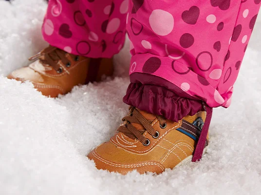 Rosa Schneehose und braune Schuhe im Schnee.