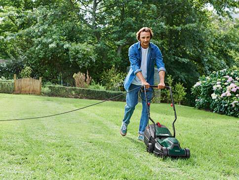 Mann mäht Rasen mit einem elektrischen Rasenmäher.
