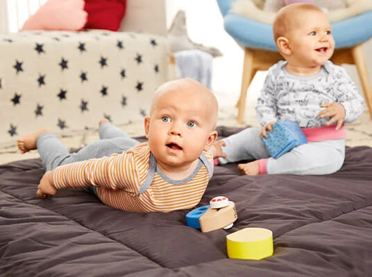 Zwei Babys spielen mit Holzspielzeug auf einer Decke.