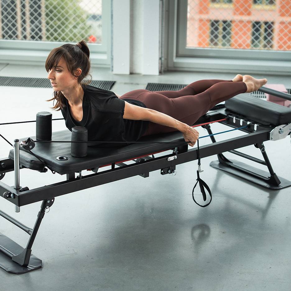 Frau trainiert auf einem Pilates-Gerät mit Widerstandsbändern.