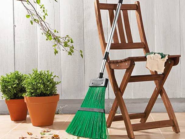 Besen und Blumentöpfe auf einem Gartenstuhl.