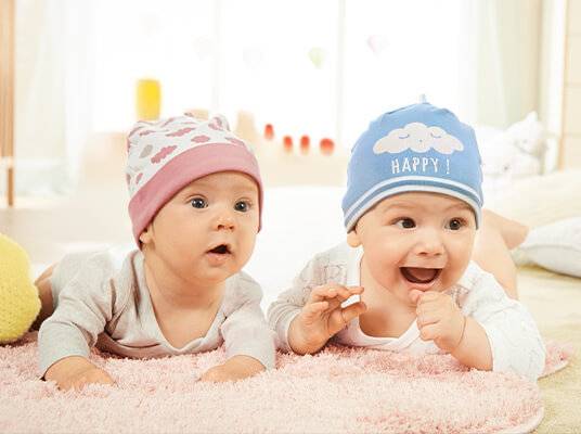 Zwei Babys in süßen Mützen: Mädchen mit Blumen- und Junge mit Wolkenmuster.