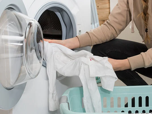 Eine Frau nimmt weiße Wäsche aus der Waschmaschine und legt sie in einen Korb.