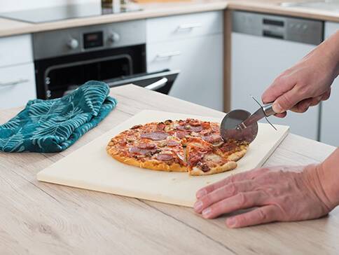Pizza, Pizzaschneider und Schneidebrett in der Küche.