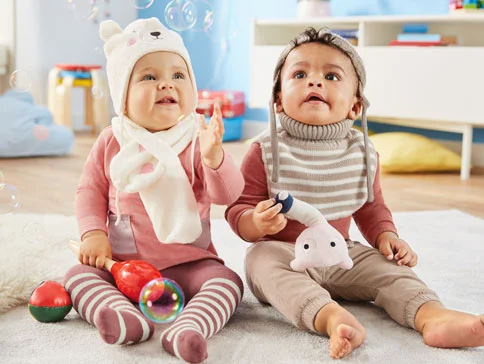 Zwei Babys in süßen Outfits und mit Spielzeug.