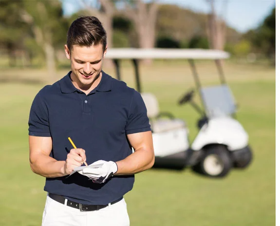 Golfer schreibt Scorekarte, Golfcart im Hintergrund.