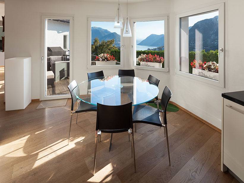 Glastisch und schwarze Stühle in einem hellen Raum mit Seeblick.