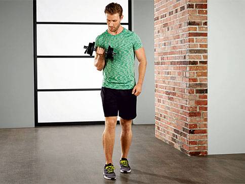 Mann trainiert mit Kurzhanteln drinnen.