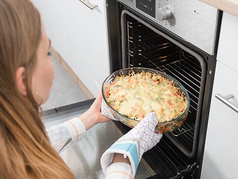 Frau nimmt käsigen Auflauf aus dem Ofen.