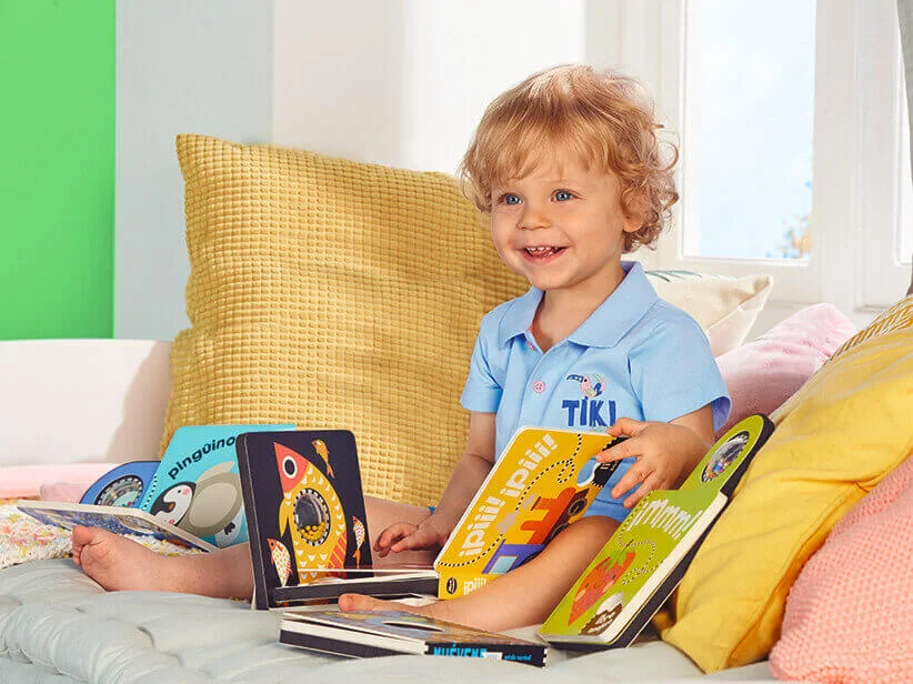 Kleinkind im Tiki-Shirt spielt mit Kinderbüchern.