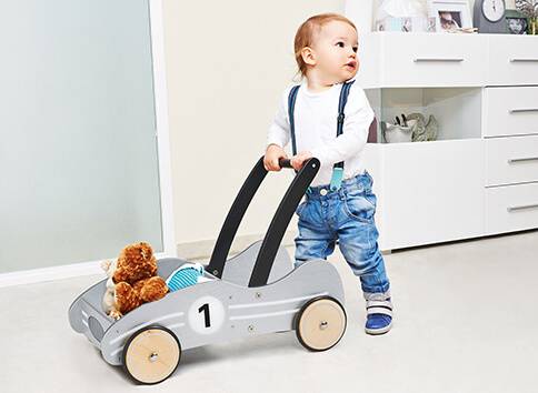 Kleinkind mit Laufwagen und Stofftieren.