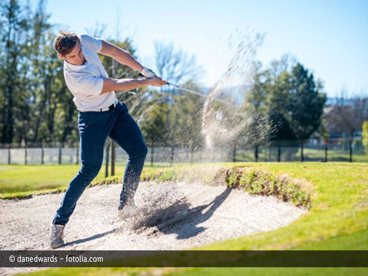Golfer schlägt Ball aus Bunker.