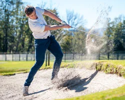 Golfer schlägt Ball aus Bunker.