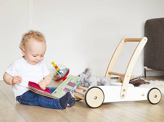 Kind spielt mit Holzwagen, Buch und Spielzeug.