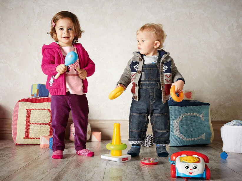 Kleinkinder spielen mit Fisher-Price Spielzeug: Rasseln und Ringsteckenspiel.
