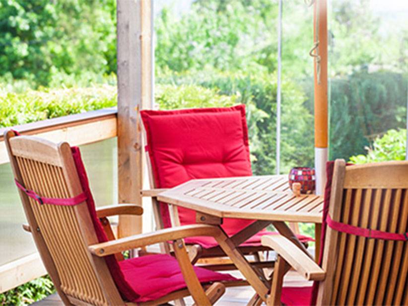 Gartenmöbel: Holztisch und -stühle, rote Kissen.