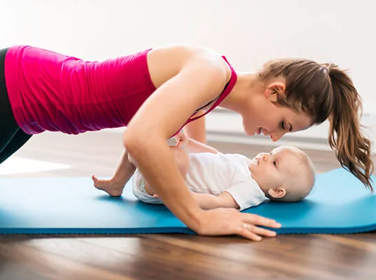Mutter trainiert mit Baby auf einer Fitnessmatte.