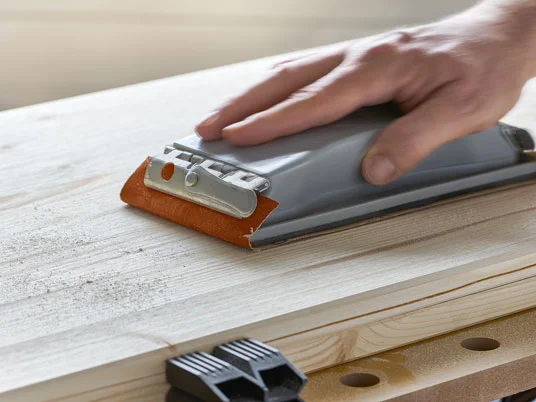 Handschleifer mit Schleifpapier glättet Holz.