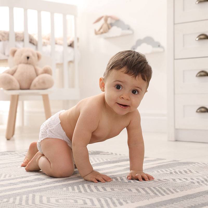 Baby in Windeln krabbelt im Kinderzimmer.