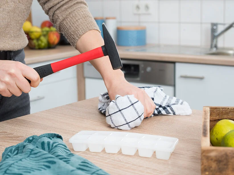 Eine Frau benutzt einen Hammer und eine Eiswürfelschale in der Küche.