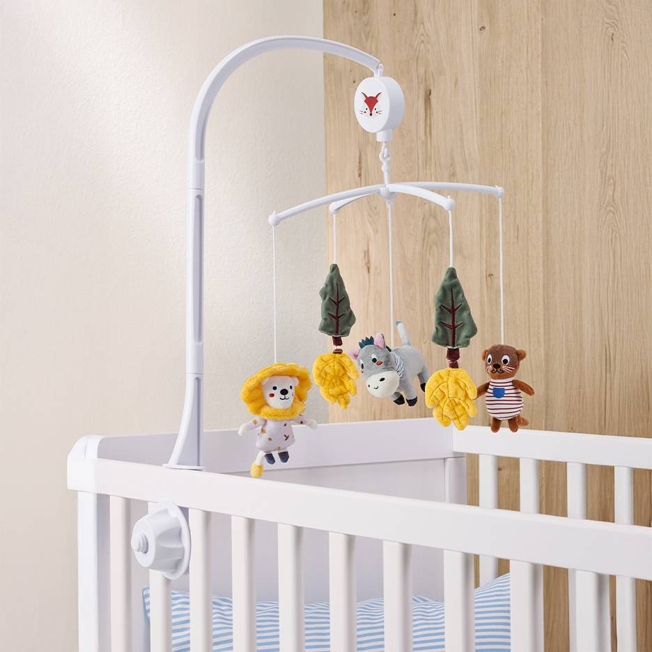 Weißes Babybett mit Mobile mit Tier- und Baumspielzeug.
