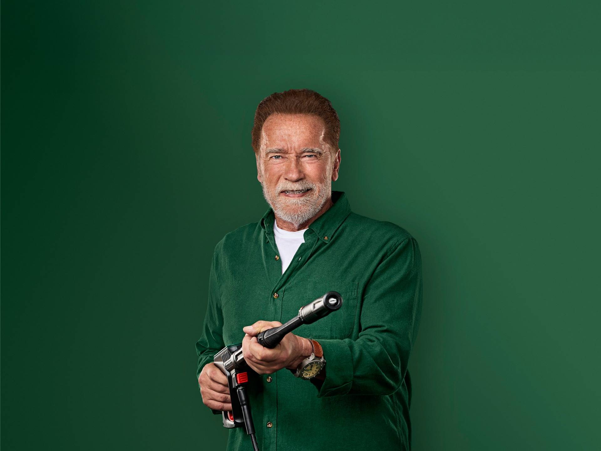 Arnold Schwarzenegger lächelt und hält eine Hochdruckreinigerpistole.