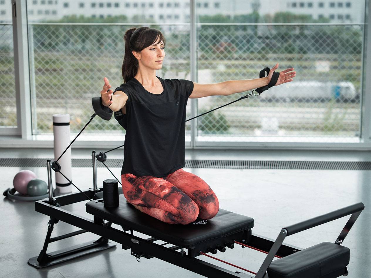 Frau macht Pilates auf einem Reformer mit Widerstandsbändern.
