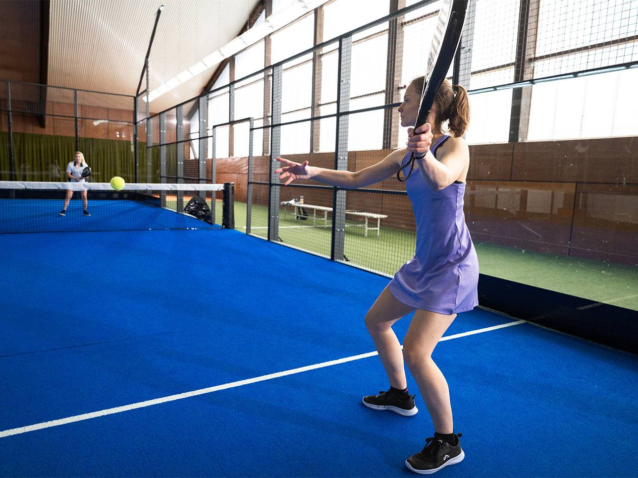 Frau in lila Sportkleid spielt Padel auf einem blauen Platz.