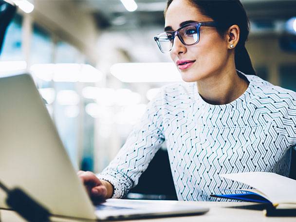 Frau arbeitet am Laptop und macht Notizen.