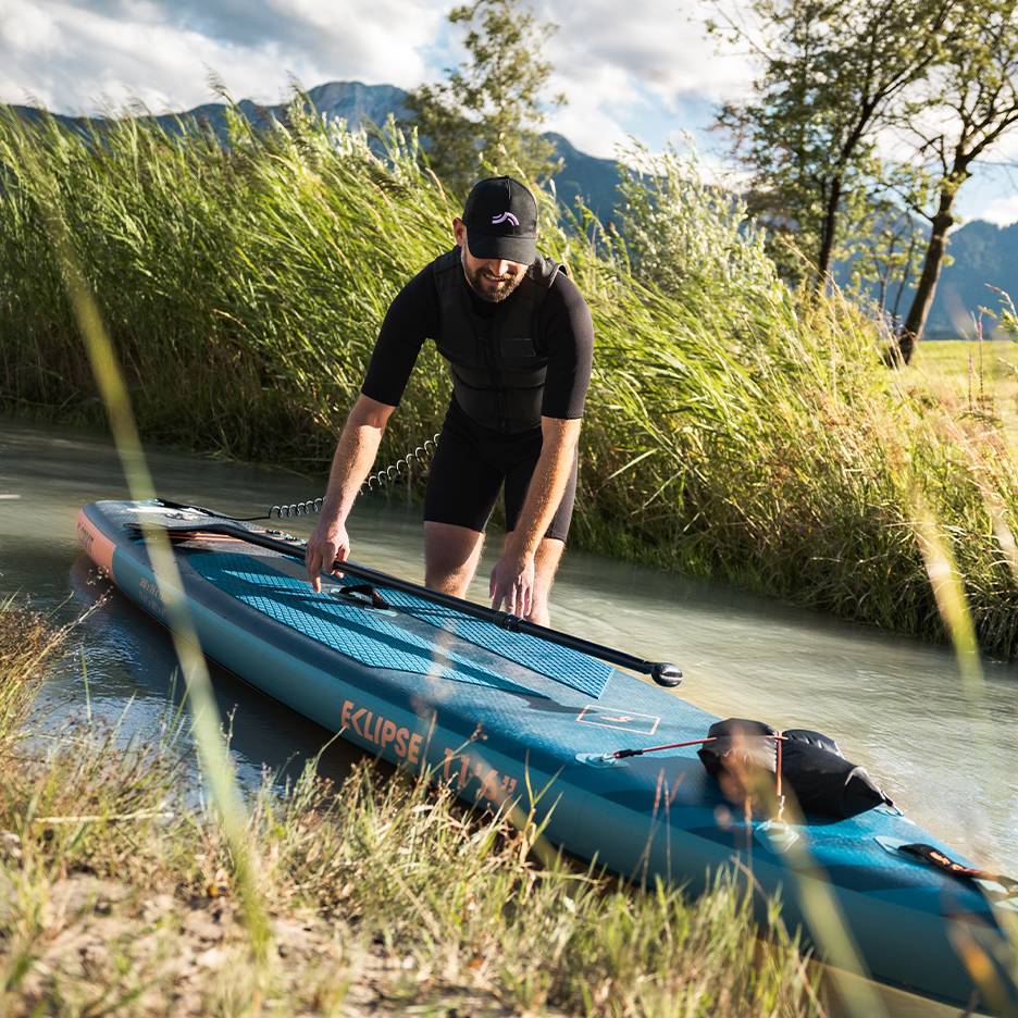 Mann in schwarzem Neoprenanzug bereitet sich auf Stand-Up-Paddling vor, Board im Wasser
