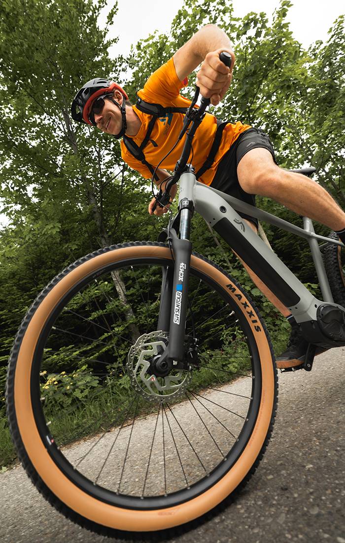 Ein Mann fährt ein graues Maxxis E-Bike durch einen Wald.