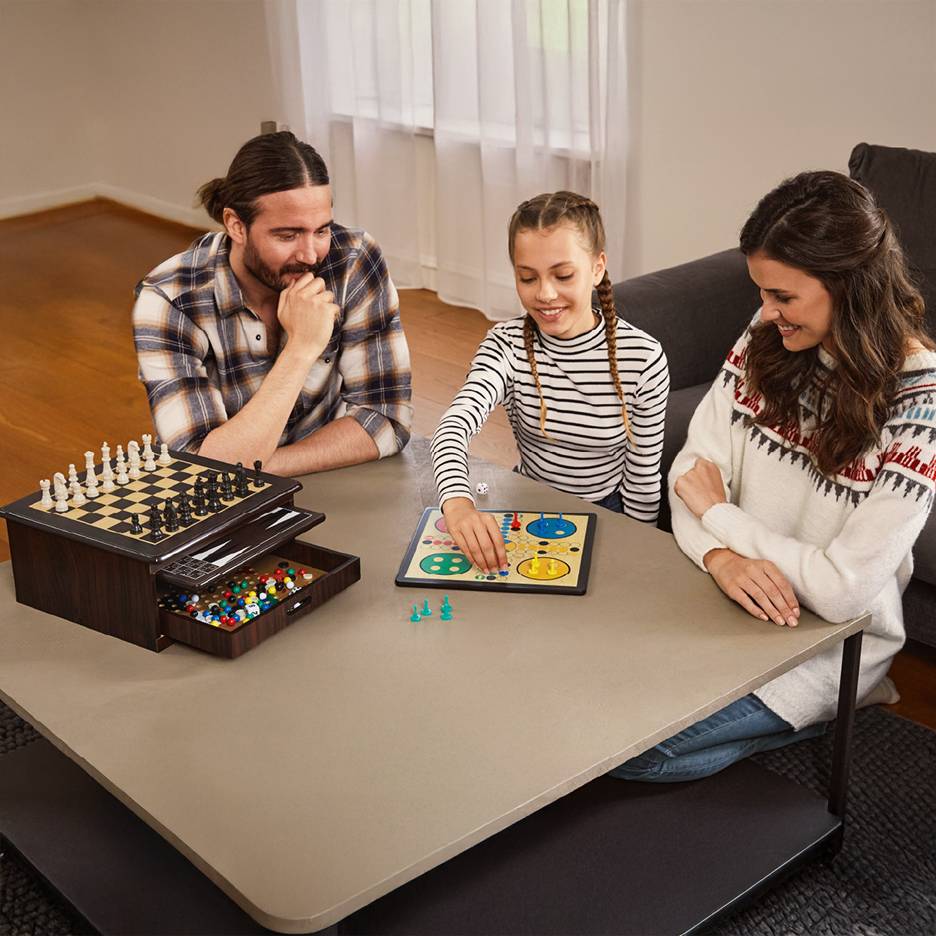 Familie spielt Brettspiele, darunter Schach und Ludo, an einem Couchtisch.