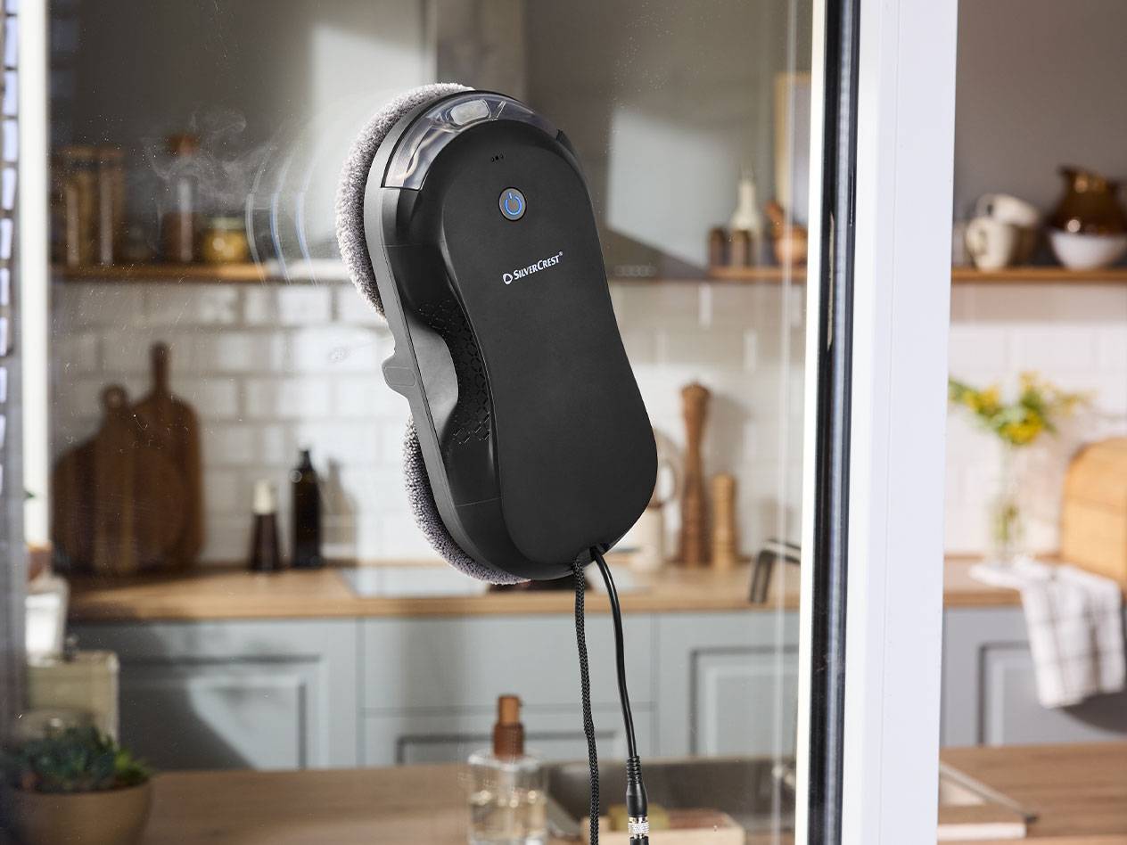 Silvercrest Fensterputzroboter an einer Fensterscheibe mit Küche im Hintergrund.