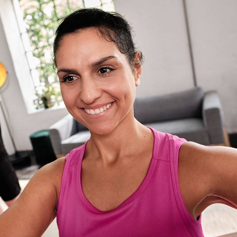 Lächelnde Frau in rosa Tanktop trainiert zu Hause.