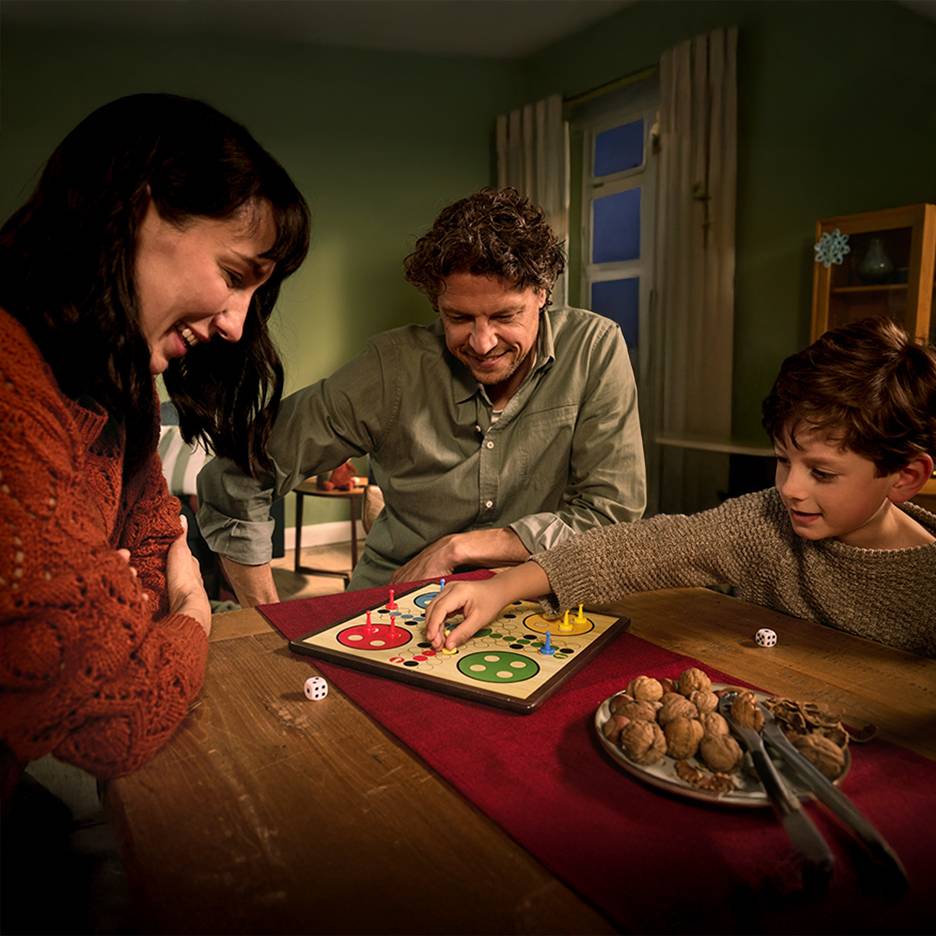 Eine Familie spielt ein Brettspiel mit Nüssen und zwei Würfeln auf einem Tisch.