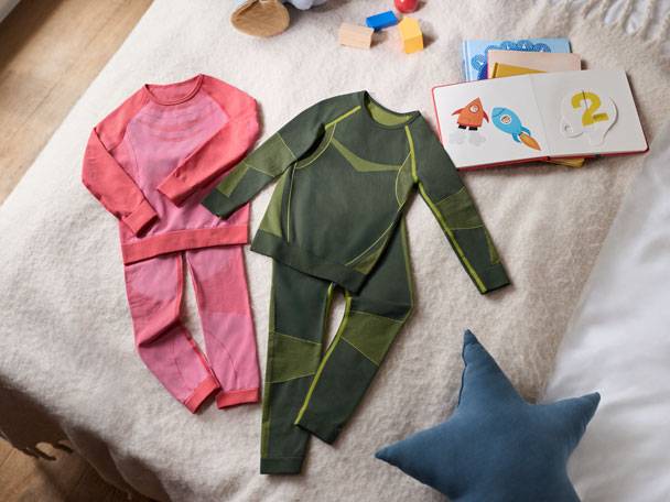 Zwei Sets Kinderunterwäsche (rosa und grün) und ein Buch auf dem Bett.