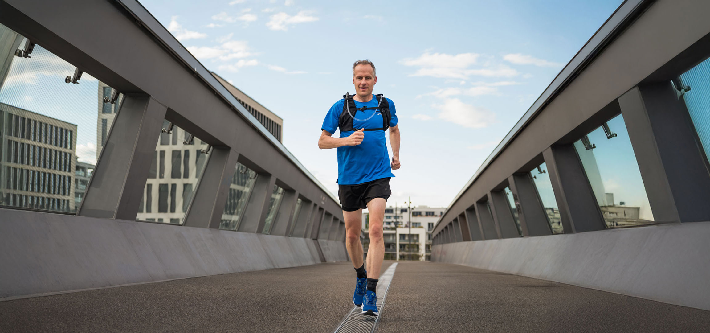 Läufer mit Laufrucksack joggt über eine moderne Brücke.