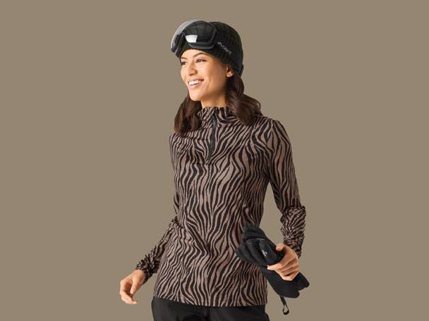 Frau in Zebra-Skioberteil, schwarzer Skimütze, Skibrille und Handschuhen.