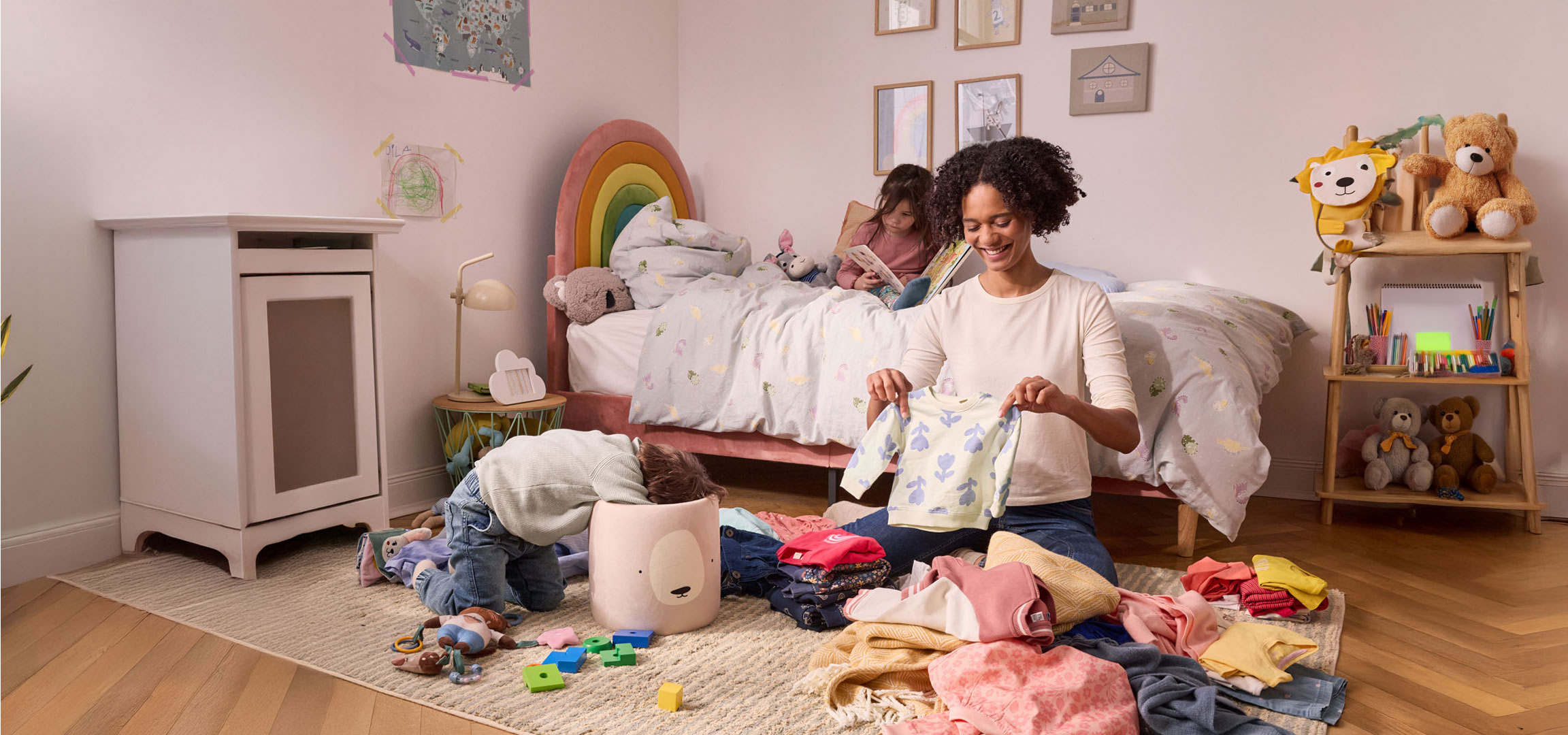 Eine Mutter räumt Kinderkleidung in einem Kinderzimmer auf.
