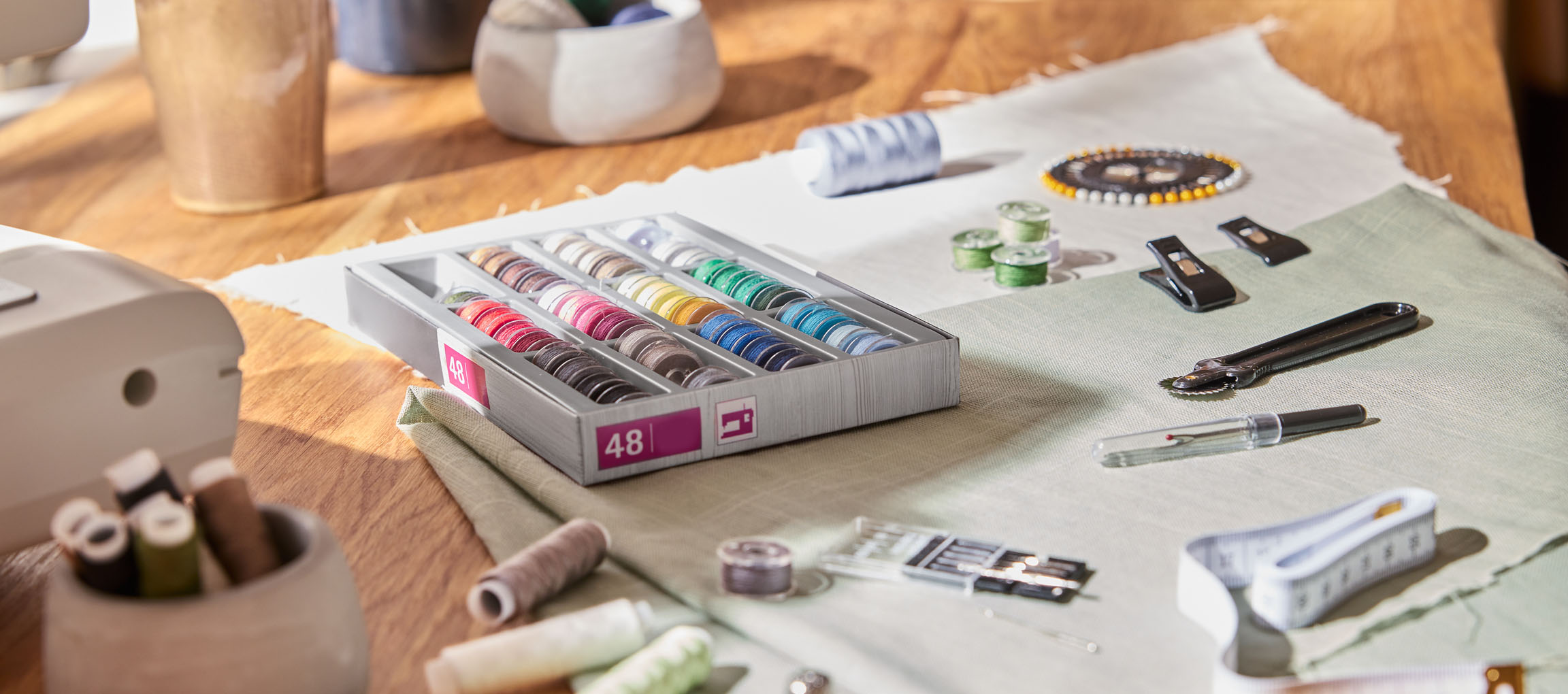 Nähzubehör auf einem Holztisch, darunter ein Garn-Organizer mit 48 Spulen, Stoff und verschiedene Werkzeuge.