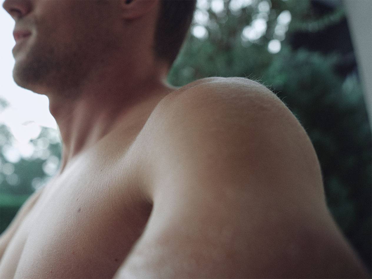 Nahaufnahme von Schulter und Hals eines Mannes, mit verschwommenem grünem Hintergrund.