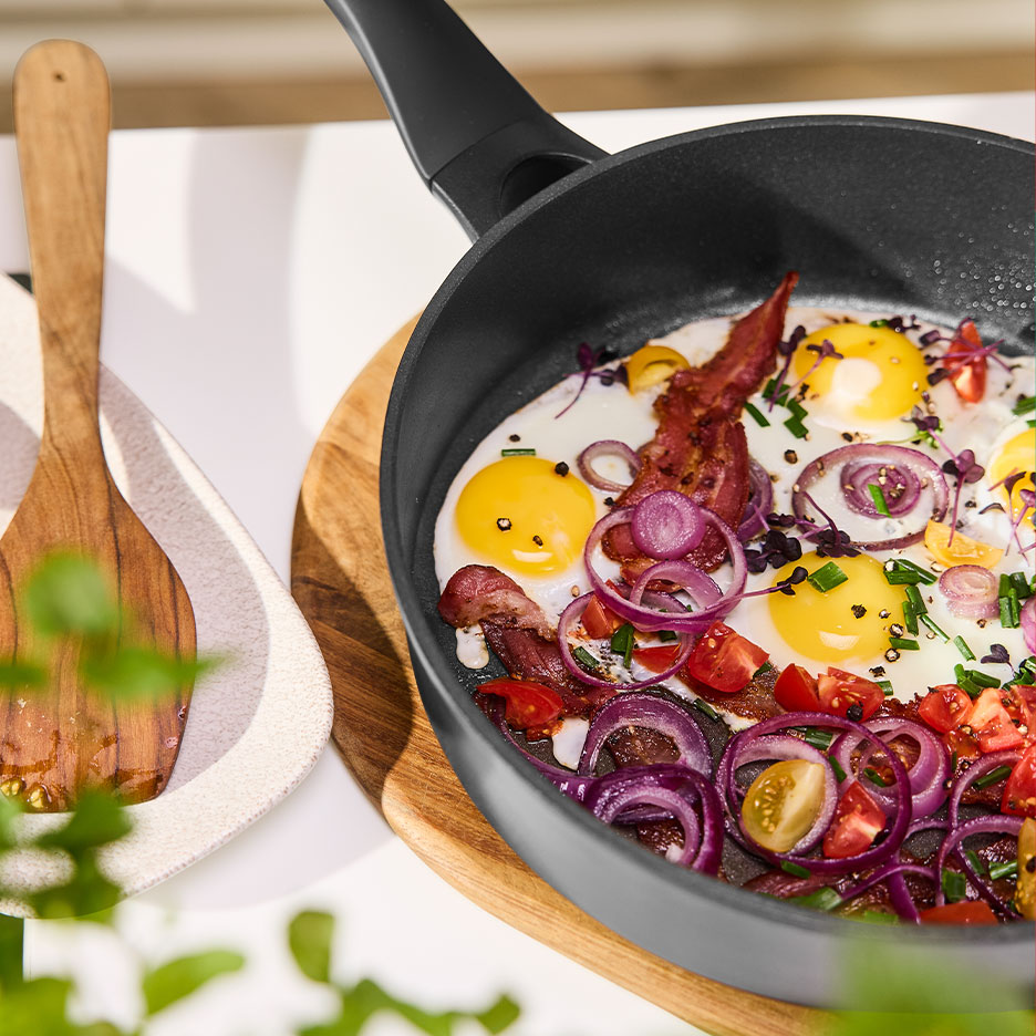 Bratpfanne mit Spiegeleiern, Speck, roten Zwiebeln und Tomaten.