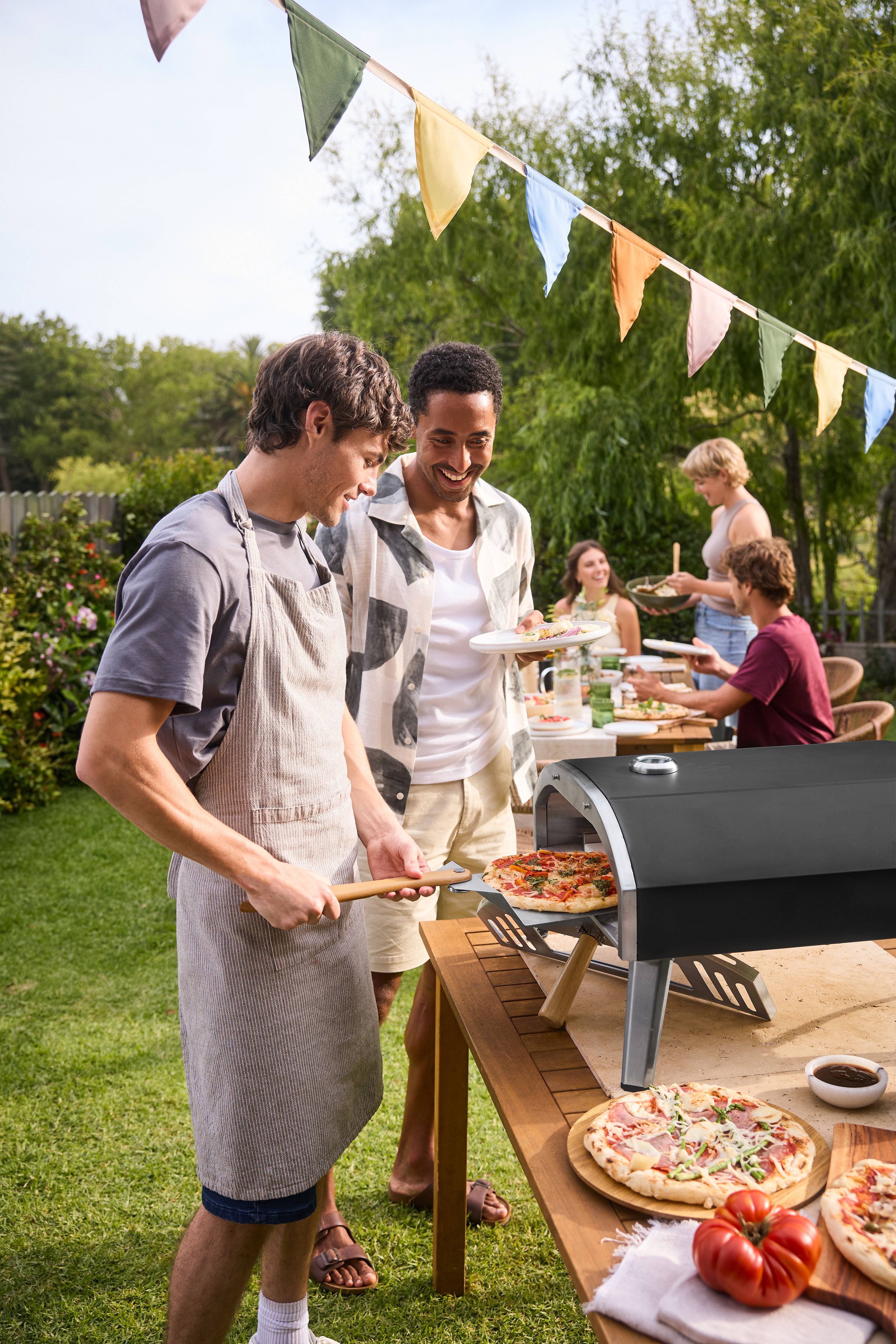 Männer backen Pizza in einem Pizzaofen auf einer Gartenparty.