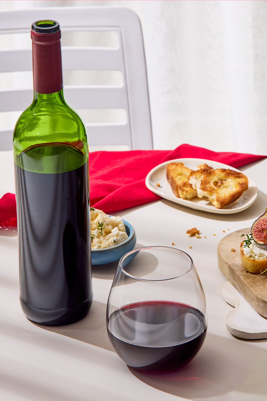 Flasche und Glas Rotwein mit Käse, geröstetem Brot und Feigen.