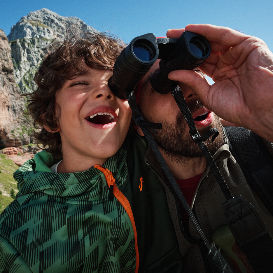 Vater und Sohn erkunden Berge mit Fernglas, tragen Outdoor-Jacken.